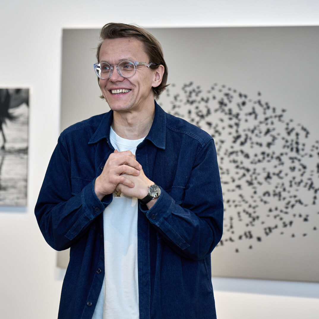 Pavlo Mazai näituse kaaskuraator Toomas Järvet Pavlo Mazai näitusel Pavlo Mazai fotode tasutal kõnelemas. Naerataval näol ja kaks kätt rinnal koos.
